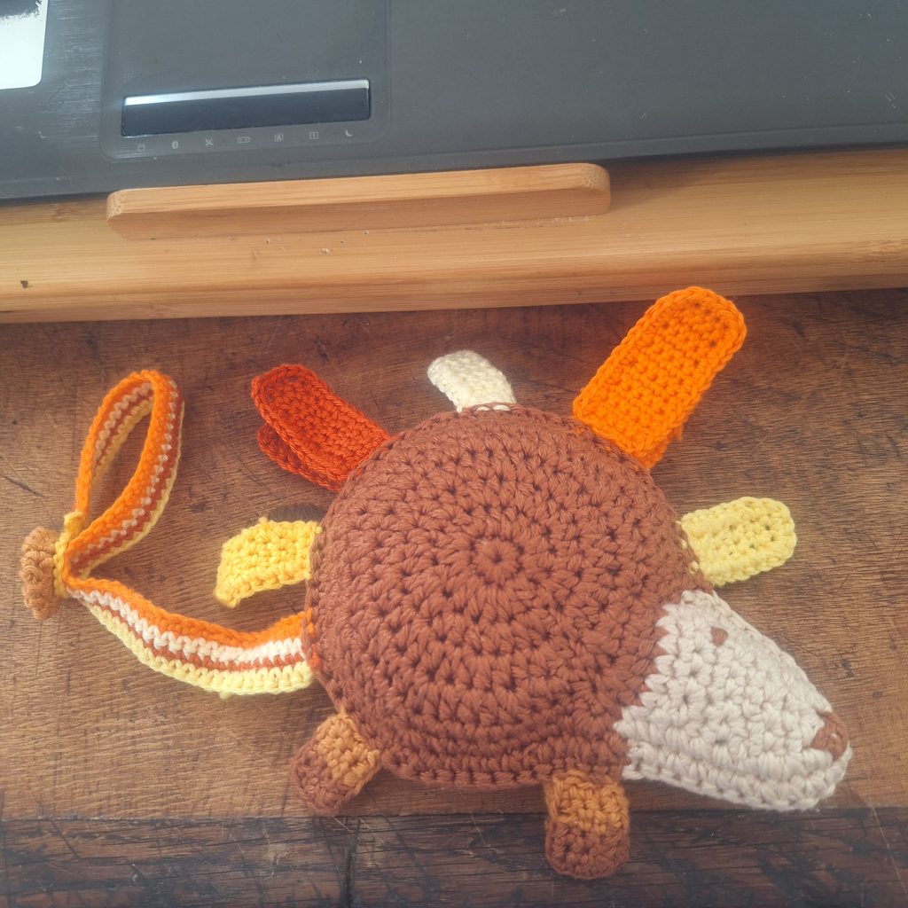 Doudou hérisson crocheté à la main, avec étiquettes colorées et pattes ajoutées.