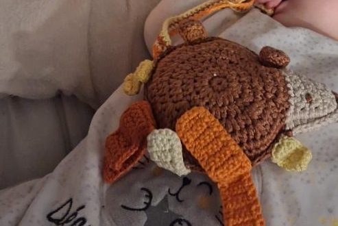 Doudou personnalisé au crochet, marron avec des étiquettes en camaïeu oranges et jaunes.