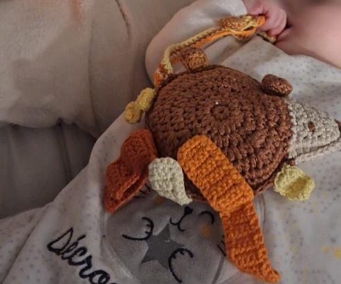 Doudou personnalisé au crochet, marron avec des étiquettes en camaïeu oranges et jaunes.