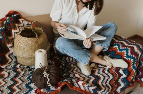 photo issue de pexels, montrant une femme feuilletant un livre de modèles au crochet pour débuter ou continuer un ouvrage. Des bobines de fils sont posées à ses côtés.